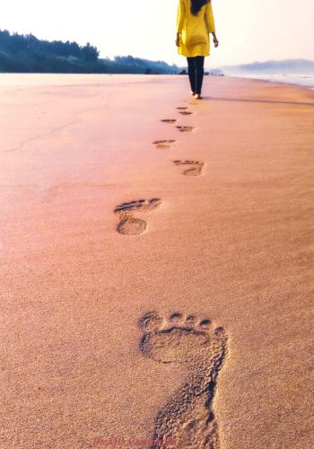 pegadas na areia e uma mulher caminhando