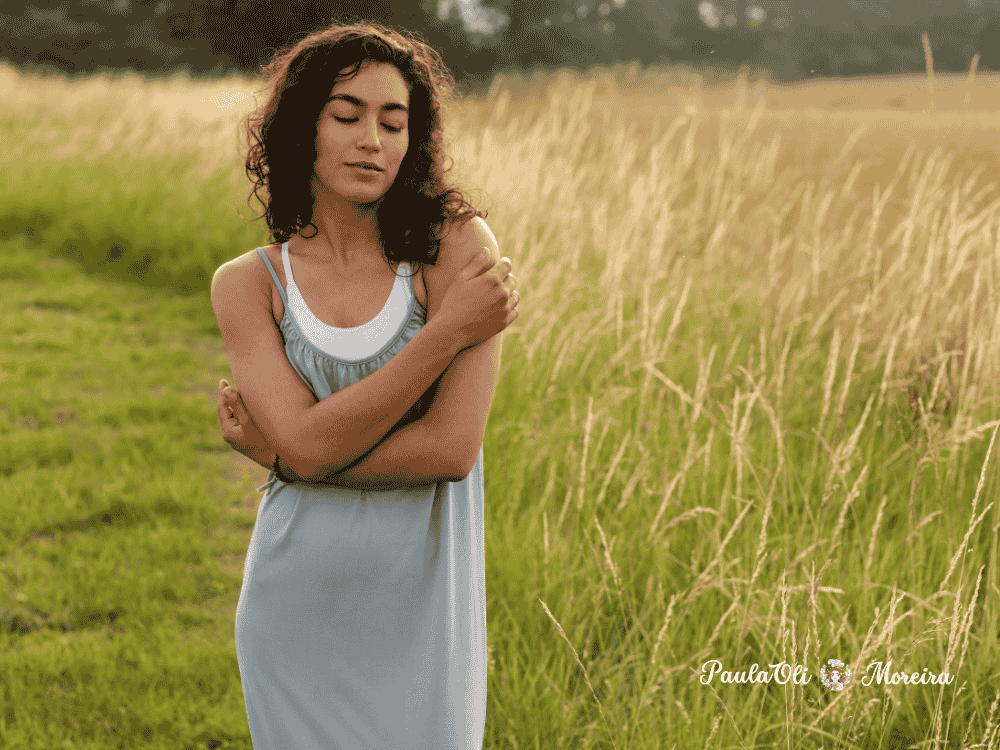 Mulher parda se abraçando em campo de trigo representando a autoaceitação-Autossabotagem-Imagem:Canva